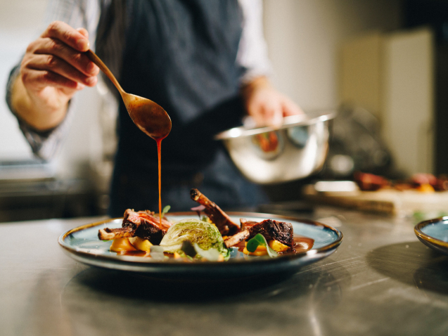 The chef pouring special sauce on pork ribs in the kitchen
